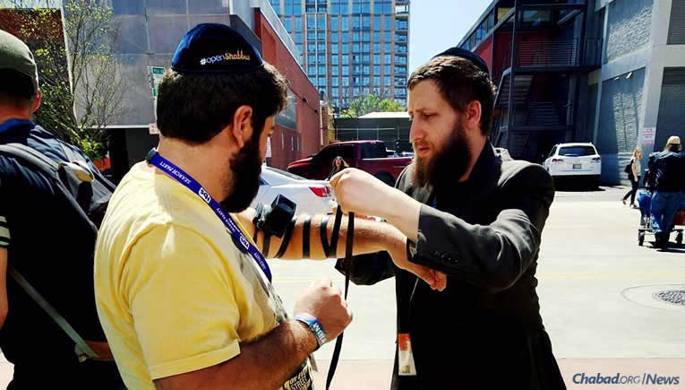 Rabbi Mordechai Lightstone, founder of Tech Tribe with his wife, Chana, wraps tefillin last year with a Jewish man at SXSW in Austin, Texas. They have been hosting an electronics-free Shabbat dinner at the festival since 2010; this year, a Purim party is also on tap, co-sponsored with local Chabad emissaries, the Levertovs, and Israel Bonds.