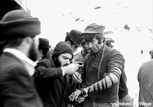 A Chabad Chassid puts on tefillin with an Israeli soldier on a military base in the 1970s. (Photo: JEM/The Living Archive)