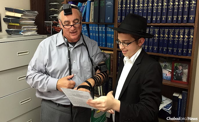 Shmuli Marozov, a student at Lubavitch Yeshivah-Zekelman Campus in Oak Park. Mich., helps Anthony Kahn put on tefillin at work. The “Friday boys,” as they are called, surpassed a goal of wrapping tefillin with 1,000 men in two months; instead, they reached nearly 1,350.