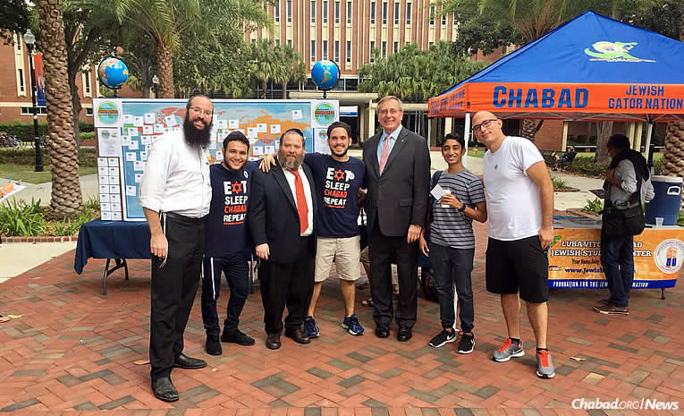 Rabbi Aharon Chaim Notik, left, co-program director at the Tabacinic Lubavitch Chabad Jewish Student Center at the University of Florida in Gainesville; Rabbi Berl Goldman, third from left, co-director of the Chabad center; and university president Kent Fuchs, third from right, stand with students near a booth at the “Good Deed Marathon” on Oct. 19 to counter the presence of white supremacist Richard Spencer.