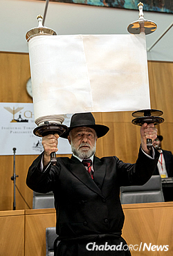 Chasia Feldman’s father, Michael Kiel of Jerusalem, lifts the Torah for all to see. (Photo: Andrew Taylor)