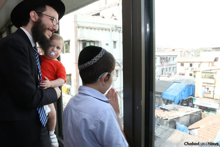 Moshe Holtzberg, right, fondly known as “Baby” Moshe, together with Rabbi Israel Kozlovsky, co-director of Chabad-Lubavitch of Mumbai, look out from Nariman (Chabad) House, as well-wishers wave and blow kisses to Moshe. (Photo: Chabad of Mumbai/Chabad.org)