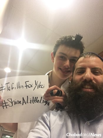 Rabbi Leibele Rodal of Friendship Circle of Montreal poses together with Matthew Mendelsohn with a #TefillinForYitzi sign.