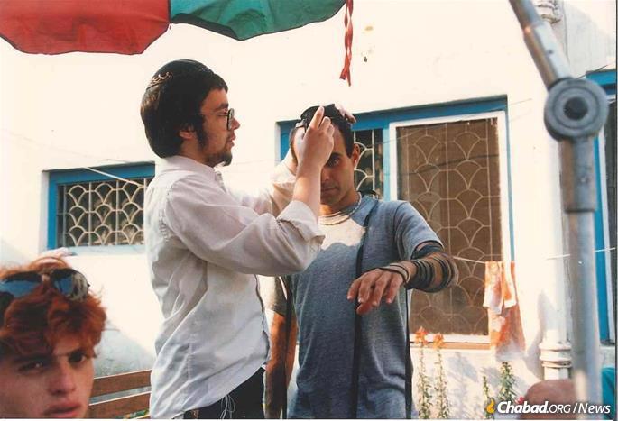 Rabbinical student Mendel Lipsker assists a backpacker with tefillin in 1989.