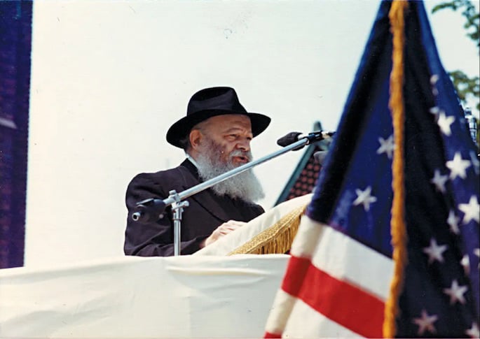 The Rebbe speaks to children at a Lag BaOmer parade in the mid 1970s. The flag of the United States of America is in the foreground.