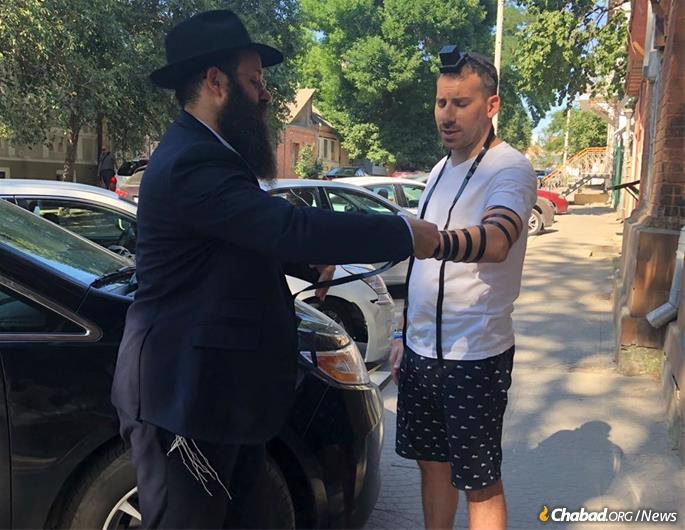 Rabbi Chaim Danzinger helps a tourist wrap tefillin and say Shema.