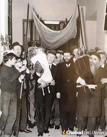 A Torah scroll welcomed to Chabad-Lubavitch of Milan, circa 1966. Rabbi Gershon Mendel Garelik is seen under the canopy, second from right. To his right holding a Torah scroll is R&#39; Mendel Futerfas, the famed Chabad Chassid who spent nine years in the Soviet gulag and later became the head mentor at the Lubavitch yeshivah in Kfar Chabad, Israel.