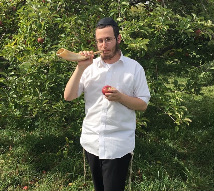 Mendel Gurary, of Bader Hillel High School, blows the shofar in the apple orchard.
