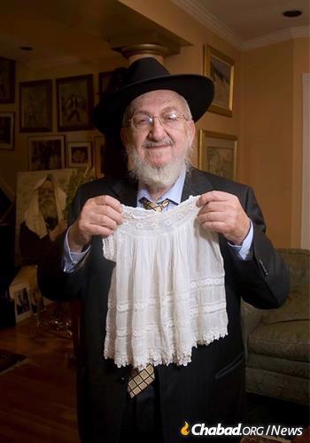 Shmuel was born during the sixth Rebbe&#39;s trip to America in 1929-30, and the Rebbe served as sandek at his bris. Fogelman poses with the outfit he wore on the Rebbe&#39;s lap. (Photo: Fogelman family collection)