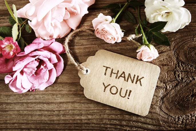 A label with Thank You written on a wooden table with a background of flowers.