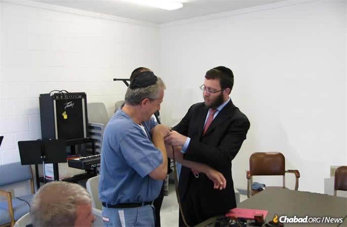 Aleph&#39;s executive director Rabbi Aaron Lipskar assists an inmate in donning tefillin.