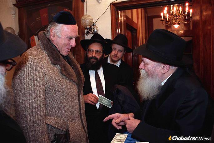Judge Jack B. Weinstein, then-chief and today senior judge on the U.S. District Court for the Eastern District of New York, receives a dollar and a blessing from the Rebbe—Rabbi Menachem M. Schneerson, of righteous memory—on Dec. 17, 1989, as Rabbi Sholom Lipskar, founder of the Aleph Institute, looks on. Weinstein was on his way to testify before the Federal Sentencing Commission. (Photo: Jewish Educational Media/The Living Archive.)