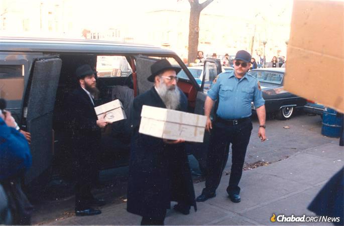 Rabbi Dovid Raskin, center, with a box of books being returned to the Library of Agudas Chasidei Chabad.