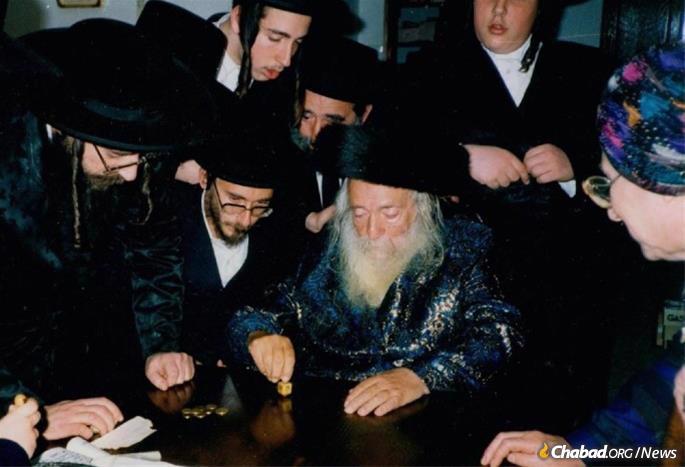 Rebbetzin Halberstam, far right, looks on as her husband spins a dreidel on Chanukah.