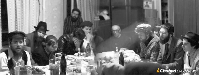 Rabbi Dovid Weitman (left) leads a farbrengen for young Jews in Leningrad in 1983. Kogan is second from the left, while R' Refael Neyomitn sits at the head of the table.