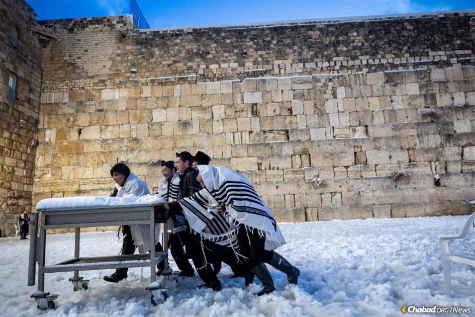 Worshippers at the Kotel (Western Wall) move a table used for Torah reading through the snow. (Photo: Yonatan Sindel/Flash90)