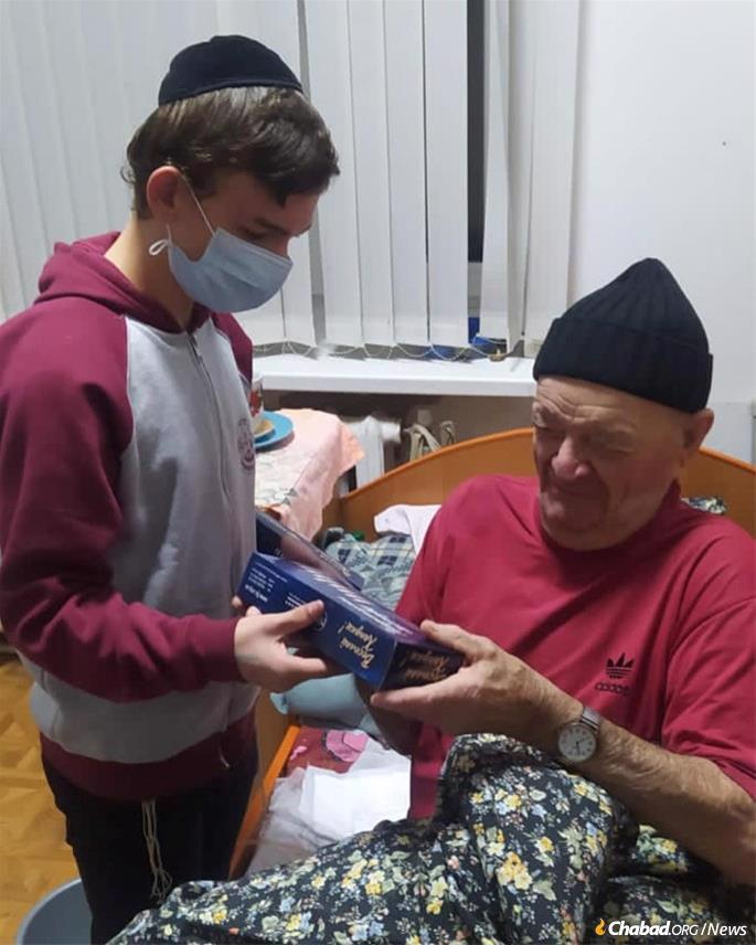 Un adolescent bénévole donne un kit de ménorah de ‘Hanouka à un Juif ukrainien âgé.