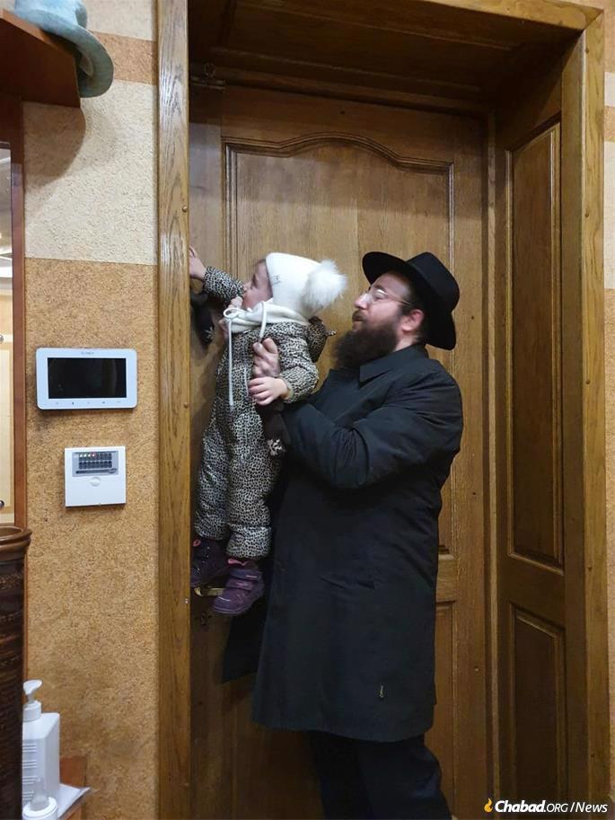 In Chernovitz, Rabbi Mendy Glitsenstein helps his child kiss the mezuzah as they flee from the city.