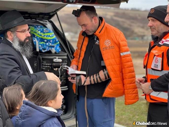 A paramedic with United Hatzalah puts on tefillin in the parking lot of a gas station in Moldova after the medics met Rabbi Yechiel Shlomo Levitansky and his family.