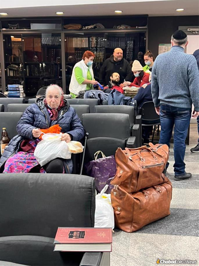 An elderly woman sits with her suitcases in the sanctuary of Chabad of Dnipro&#39;s Golden Rose Synagogue as another refugee receives medical care in the background. (Photo: Dnipro Jewish Community)