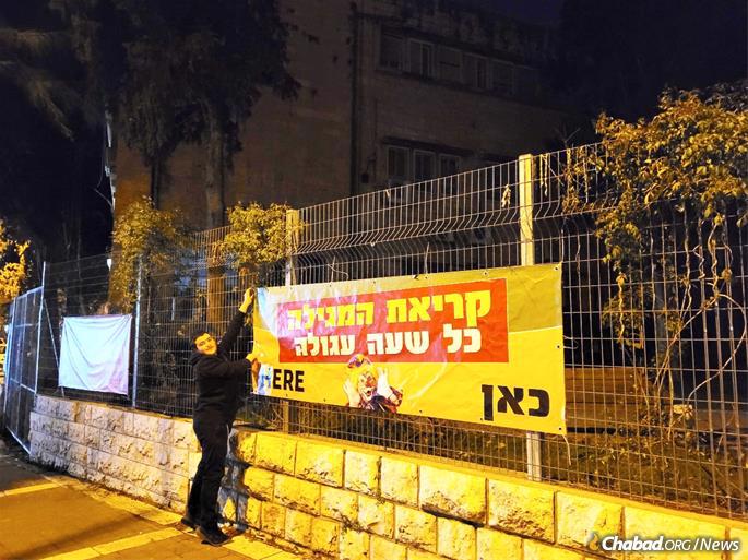Mendel Goldberg of Chabad of Rechavia putting up a banner of Azza Zaza nonstop Megillah readings at the entrance to the famous Gimnasia Public High School in central Jerusalem.