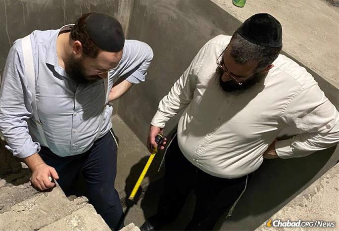 Mikvah expert Rabbi Sholom Ber Shuchat,right, examines the mikvah during construction, together with Rabbi Yaakov Raskin, left.
