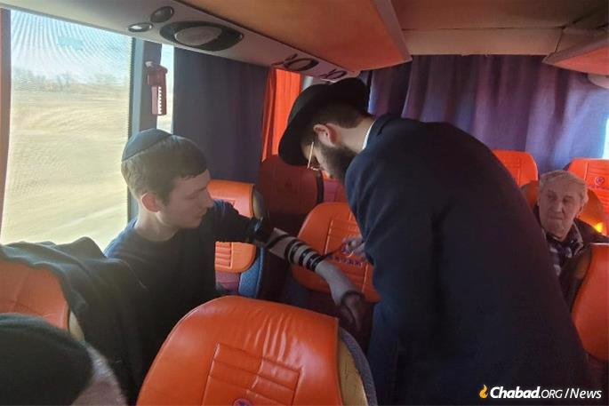 Dubi Ehrentreu helps a young man put on tefillin on the bus heading to the border.