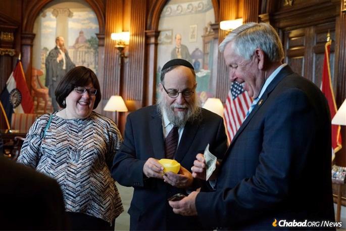 Rabbi Yosef and Shiffy Landa present an ARK (Acts of Routine Kindness) charity box to Missouri Gov. Mike Parson in honor of the 120th anniversary of the birth of the Rebbe.