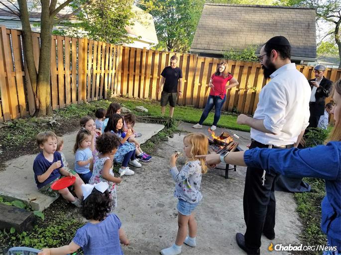 Rabbi Yaakov Dovid Kotlarsky toasts marshmallows with children at a Lag BaOmer barbecue.