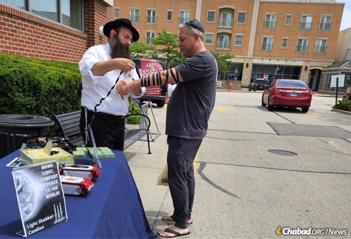 Rabbi Chaim Moshe Telsner helps a passerby put on tefillin.