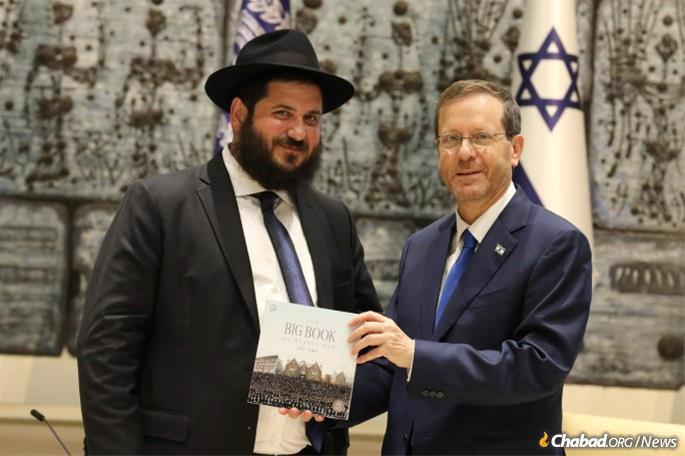Rabbi Mendy Kotlarsky, left, presents Israel&#39;s President Isaac Herzog with an album on Chabad&#39;s activities. (Credit: Israel GPO)