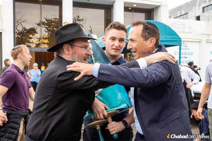 Barak Weisenberg holds the new Torah as his father, Avraham Weisenberg, and Rabbi Goodman celebrate.