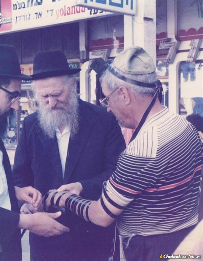 Moshe Greenberg in his older years helps someone don tefillin in Israel.