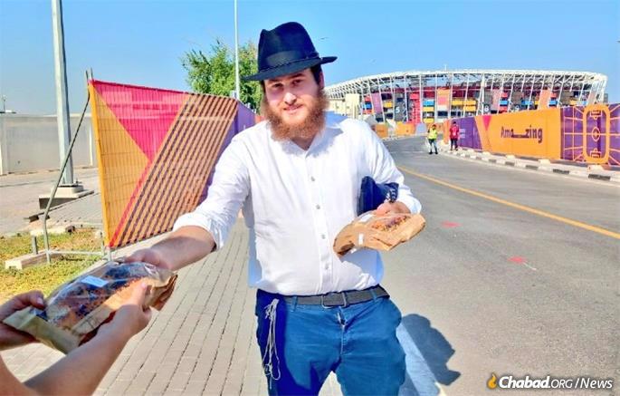On the streets of Qatar with black hat and tzitzis, Chitrik distributes a challah before Shabbat.