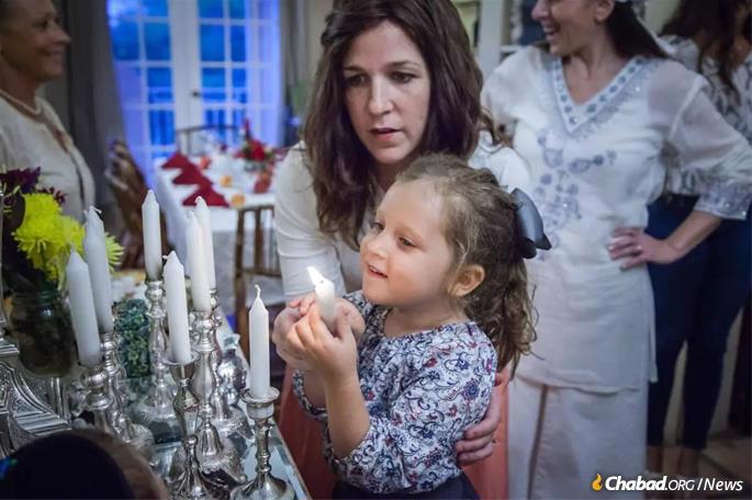 Henya Federman assists a daughter in lighting Shabbat candles.