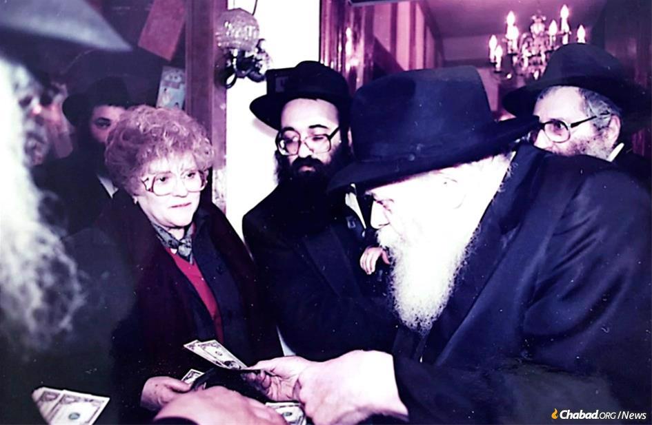 Judy Silber, accompanied by Rabbi Yitzchok Wolf (center), receives a dollar and blessing from the Rebbe, whom her family had known since she was a small child.