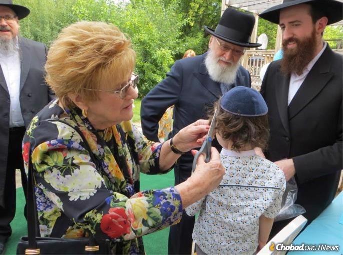 Judy Silber snips a lock of hair at the upshernish of her great-grandson, son of Yechiel Silber (right) and grandson of Mayer Silber (left), while her husband looks on.