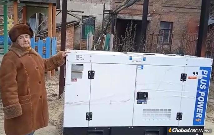 Svetlana Levovna Suprunova, an elderly resident of Sumy, Ukraine, with the new electric generator that provides heat and hot water to the Jewish communal building and the synagogue next door, which she calls her “second home.” 