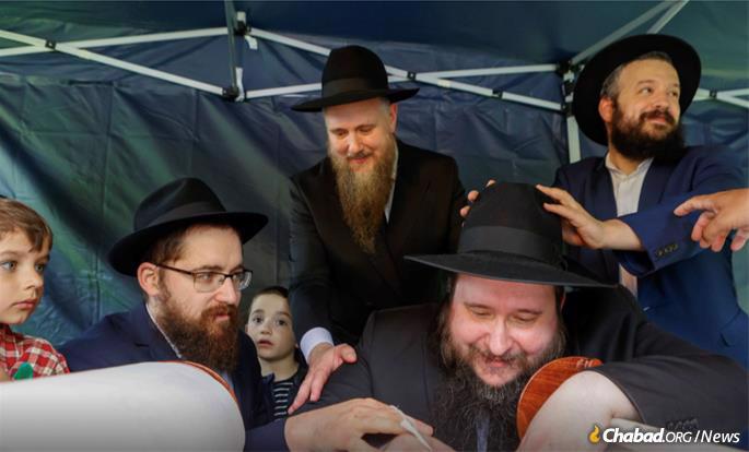 Rabbi Yitzchak Mendel Wagner, standing center, watches scribe Rabbi Yosef Dan Khranovsky complete the Torah scroll.