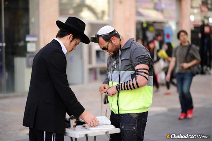 Tefillin stands are popular sites across Israel and around the world—often simply a portable table with tefillin and instructional pamphlets, as well as Shabbat candles for women, manned by volunteers who assist individuals who may need guidance with wrapping and reciting the blessing.