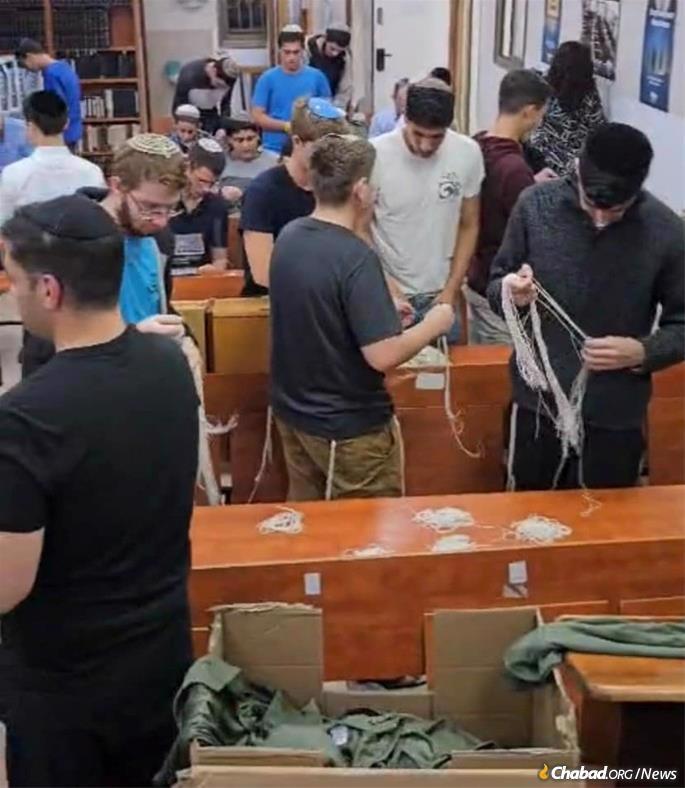 Estudantes da Yeshiv&#225; em Beersheva amarram os fios do tsitsit para serem presos a camisetas verdes militares de quatro cantos (parte inferior). Os tsitsit foram solicitados por soldados que se dirigiam para Gaza.