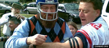 A helmeted Rabbi Yossi Deren, co-director of Chabad-Lubavitch of Greenwich, Conn., helps New York Giants fan David Katz put on tefillin at a tailgating party in Roslyn, N.Y.