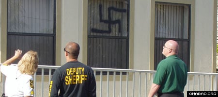 Investigators look at one of three swastikas spray-painted on a building at Chabad-Lubavitch of Parkland, Fla.