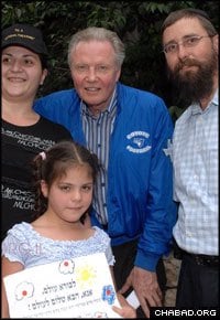 Rabbi Menachem Kutner, right, of Chabad’s Terror Victims Project accompanies American actor Jon Voight on a visit with Jerusalem’s Hondiashvili family. The little girl, whose father Baruch Hondiashvili was killed in the Jan. 29, 2004 suicide bombing of Jerusalem’s Bus No. 19, holds a letter to G-d that says: “Creator of the world, please bring peace to the world.” (Photo: Meir Dahan)