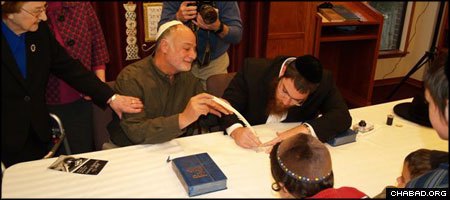 An Arkansas Jewish man participates in the state’s first-ever Torah writing by holding on to the quill as a ritual scribe fills in a holy letter.