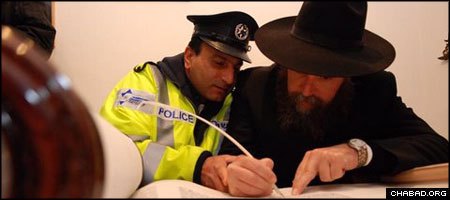 Assisted by a ritual scribe, an Israeli police officer fills in one of the last letters of a Torah scroll dedicated in memory of a Holocaust survivor who passed away without children.