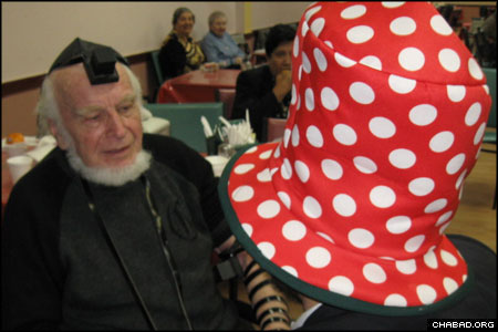Wearing an oversized hat in honor of Purim, a Chabad-Lubavitch rabbinical student assists 81-year-old Arnold Edward in donning tefillin for the first time. “We danced and sang,” related Tenenbaum. “90-year-old men were crying.”