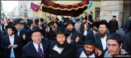 Hundreds of people crowd a Krakow street as they march with a new Torah scroll for the historic Rema Synagogue.