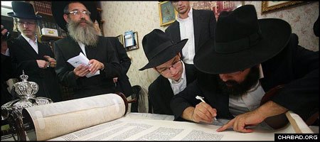Descendents of Rabbi Aharon Mendel and Nechama Leah Hazan fill in letters of a Torah scroll written in their memory.