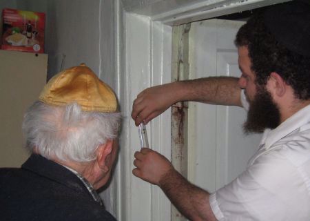Helping an elederly Jew affix a mezuzah on his door. Note the box of matzah.